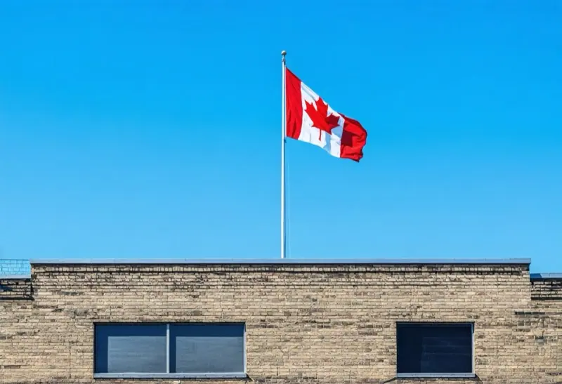 Canadian flag on a pole above the flat roof of a brick building