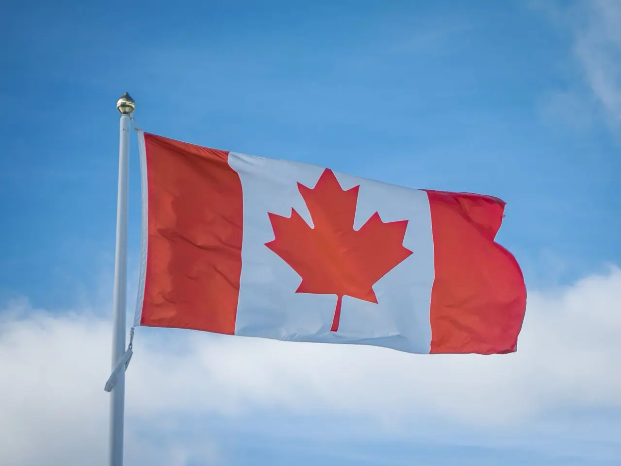 Canadian flag flying from a white flagpole against a blue sky