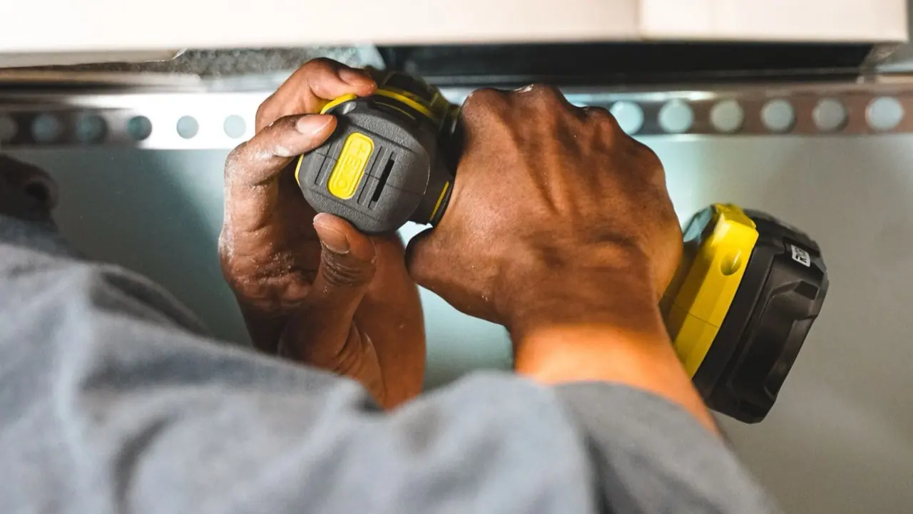 Hands using a cordless drill on metal hardware
